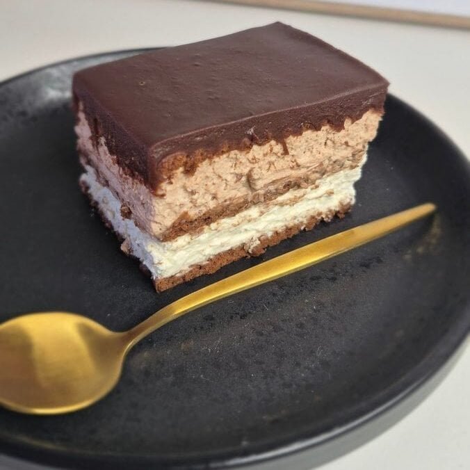 Slice of no-bake chocolate biscuit cake with mascarpone filling and chocolate ganache on a black plate