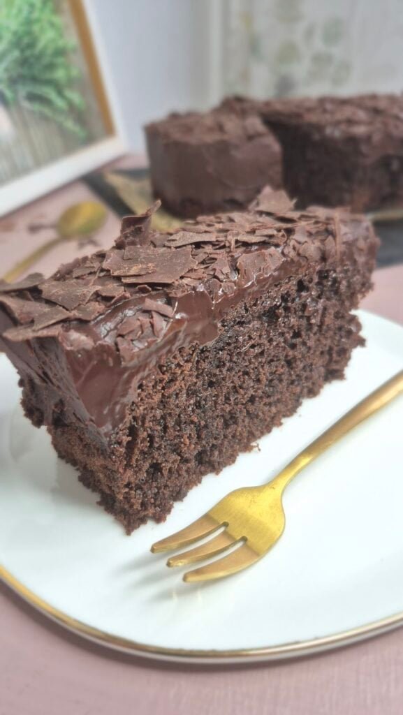 Moist chocolate cake recipe slice with smooth chocolate topping served on a white plate