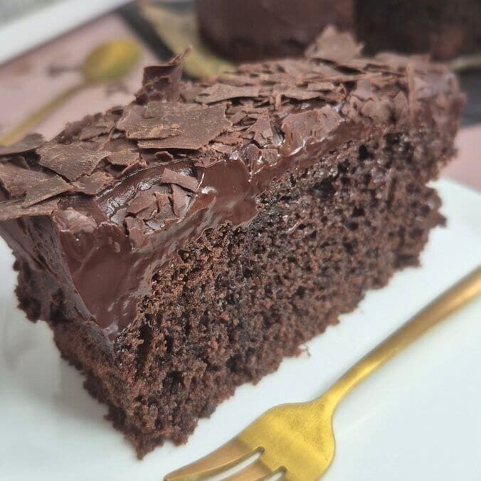 Moist chocolate cake slice with chocolate topping served on a white plate