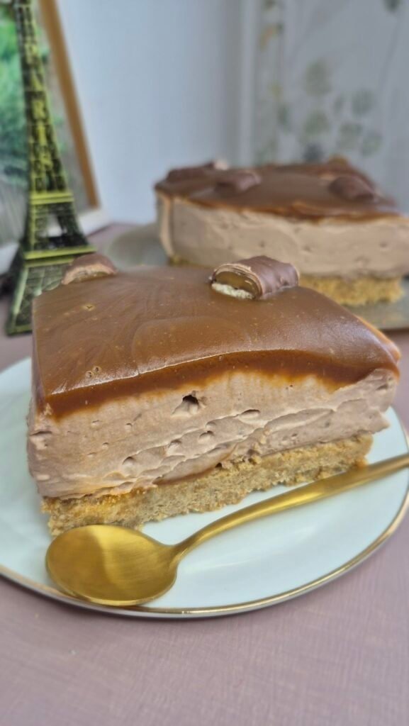 Twix caramel cheesecake slice with biscuit base, creamy mascarpone filling, and smooth caramel topping on a plate