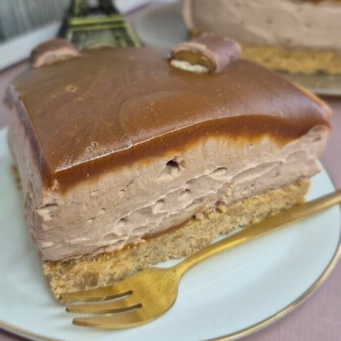 Twix caramel cheesecake slice on a white plate, with biscuit base, creamy filling, and glossy caramel topping