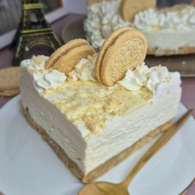 Golden Oreo cheesecake slice topped with mascarpone cream and Golden Oreo cookies on a white plate