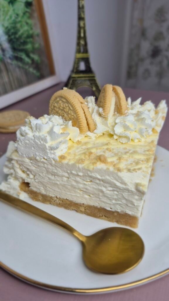 Golden Oreo cheesecake slice with cream topping and cookie pieces served on a white plate