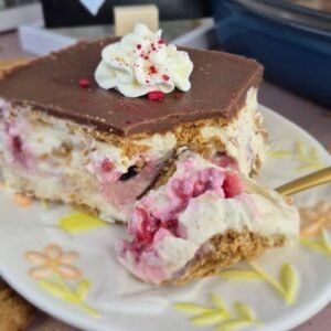 Slice of biscuit cake with mascarpone cream, raspberries, blueberries, banana and chocolate ganache on a plate