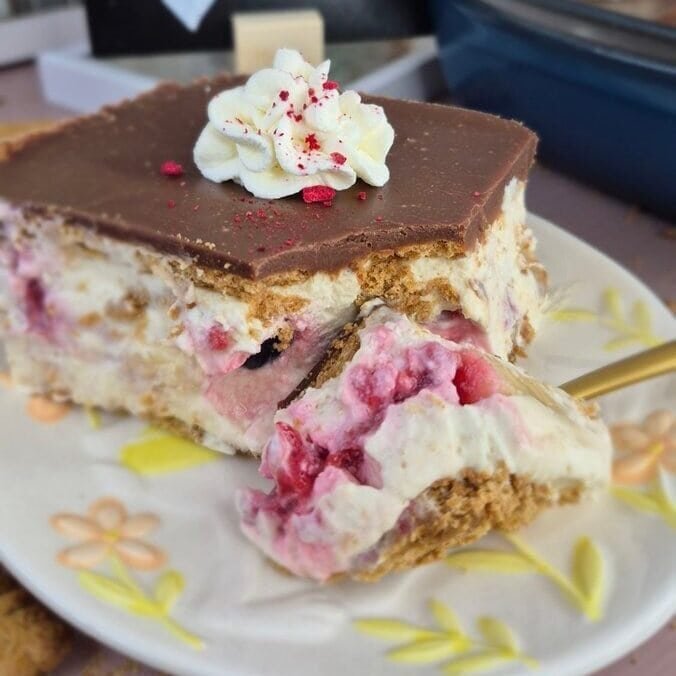 Slice of biscuit cake with mascarpone cream, raspberries, blueberries, banana and chocolate ganache on a plate