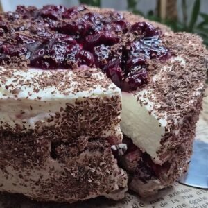 Slice of no-bake Black Forest cake with chocolate biscuit base, mascarpone filling, cherry topping, and grated chocolate