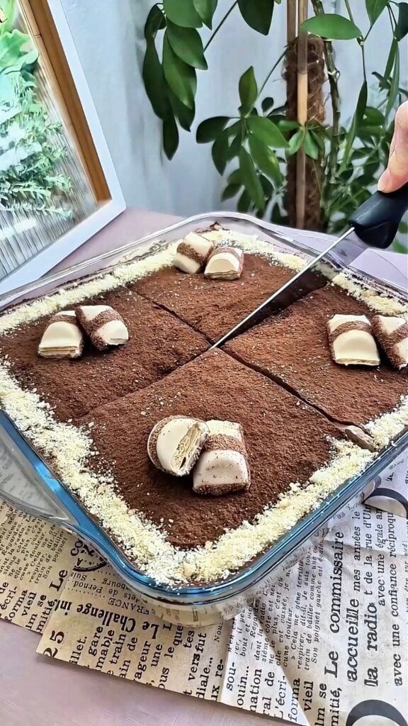 Kinder Bueno tiramisu in a glass dish topped with cocoa powder and halved Kinder Bueno pieces