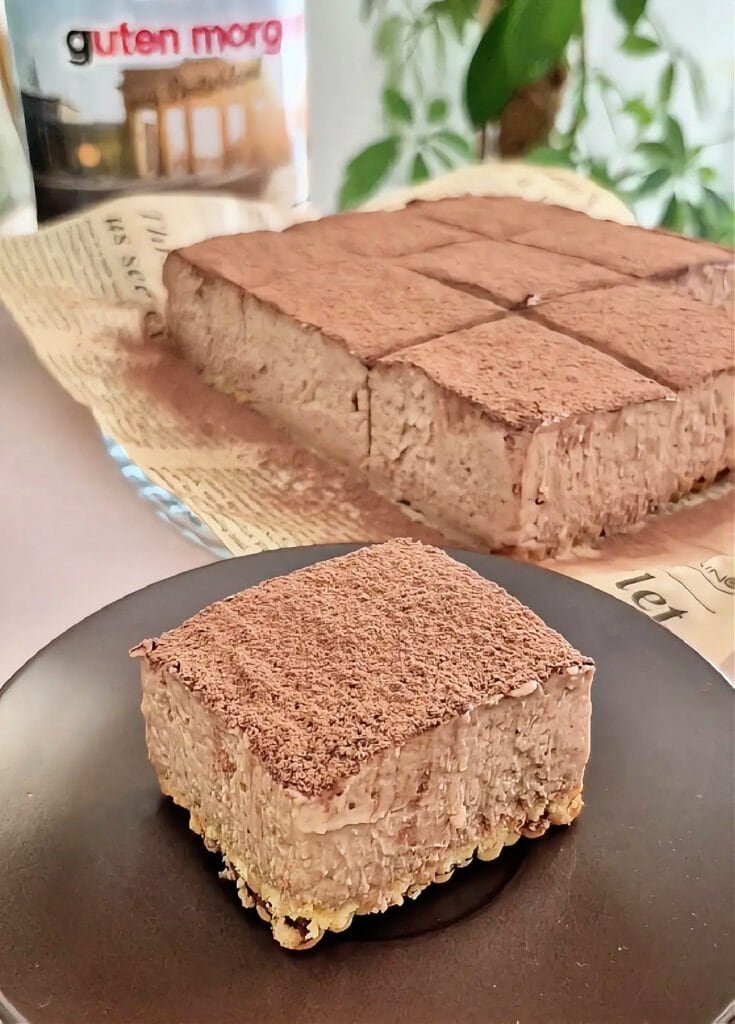 Nutella tiramisu squares in a pan with a cocoa-dusted top and one square served on a plate