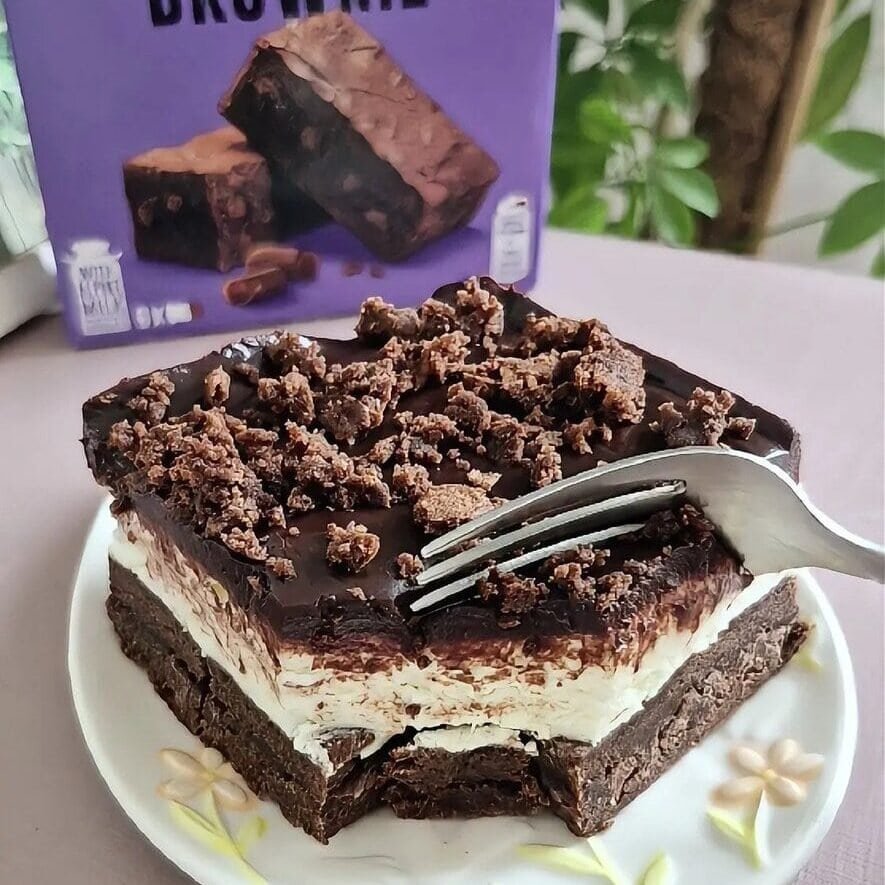 Slice of no-bake Milka brownie cake with mascarpone cream and chocolate ganache, served on a plate with a fork