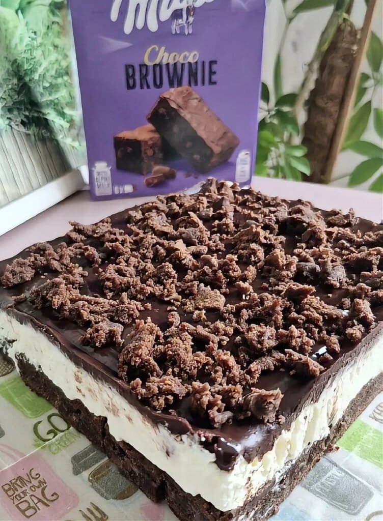 Whole no-bake Milka brownie cake with mascarpone cream layer and chocolate ganache topping in a dish.