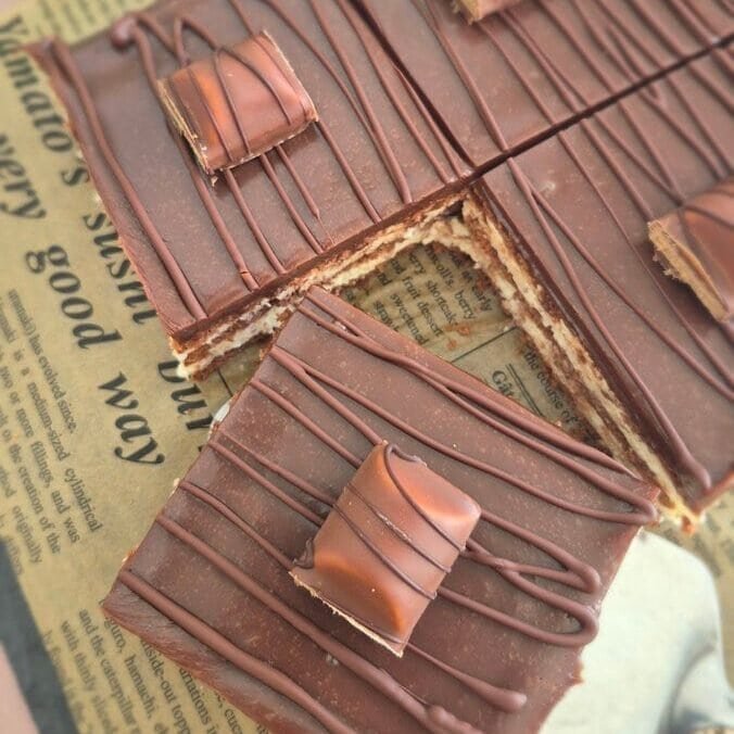 Kinder Bueno bars topped with chocolate drizzle and Kinder Bueno pieces, cut into squares and arranged on parchment paper.