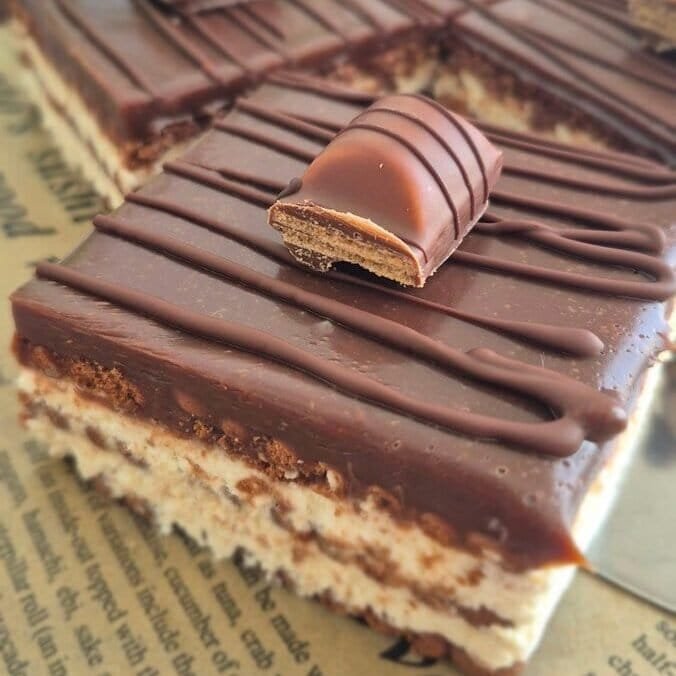 Kinder Bueno bars with cocoa biscuit layers, mascarpone filling, chocolate topping, and a Kinder Bueno piece on top.