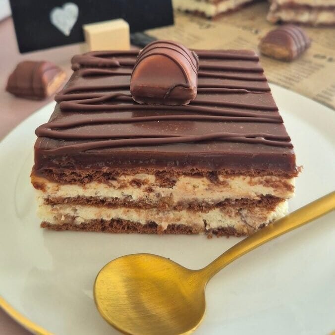 Kinder Bueno bars with layered mascarpone filling and chocolate topping on a white plate, with a spoon in the foreground.