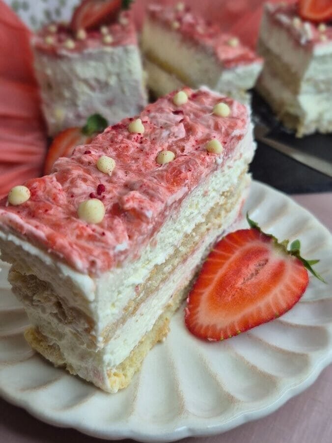Slice of strawberry tiramisu cake on a white plate with mascarpone cream layers, ladyfingers, and fresh strawberry on top