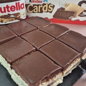 Square no-bake Kinder Cards cake with creamy white filling and smooth chocolate ganache cut into slices, with Kinder Cards and Nutella jars in the background.