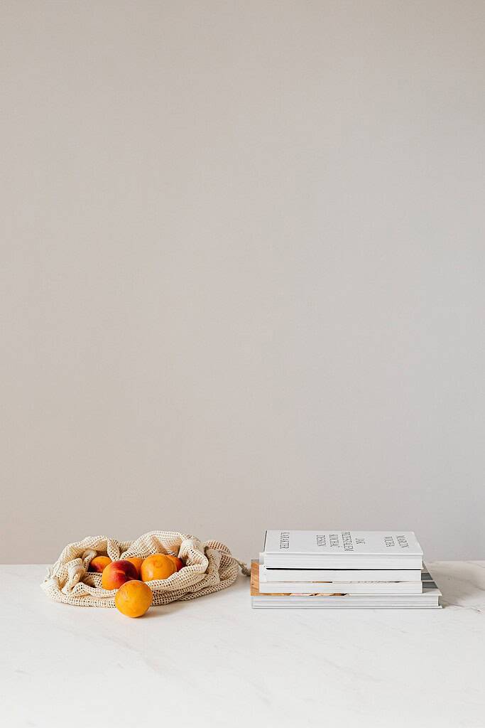 A photograph of a styled scene. There is a market bag with oranges on the left, and a pile of four books on the right. This is to represent the article listing 18 literary magazines accepting submissions.