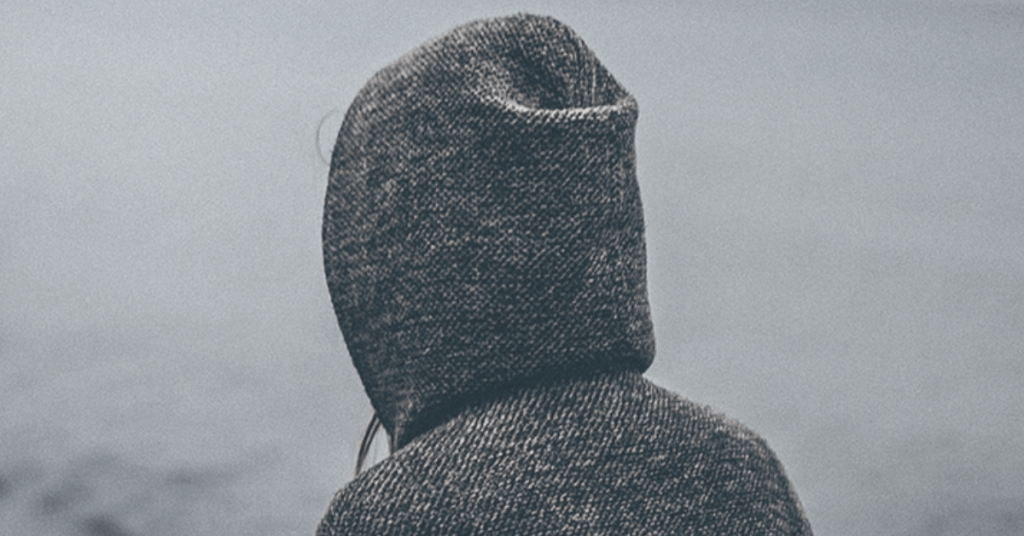 woman with hood up stares up at grey, cloudy sky