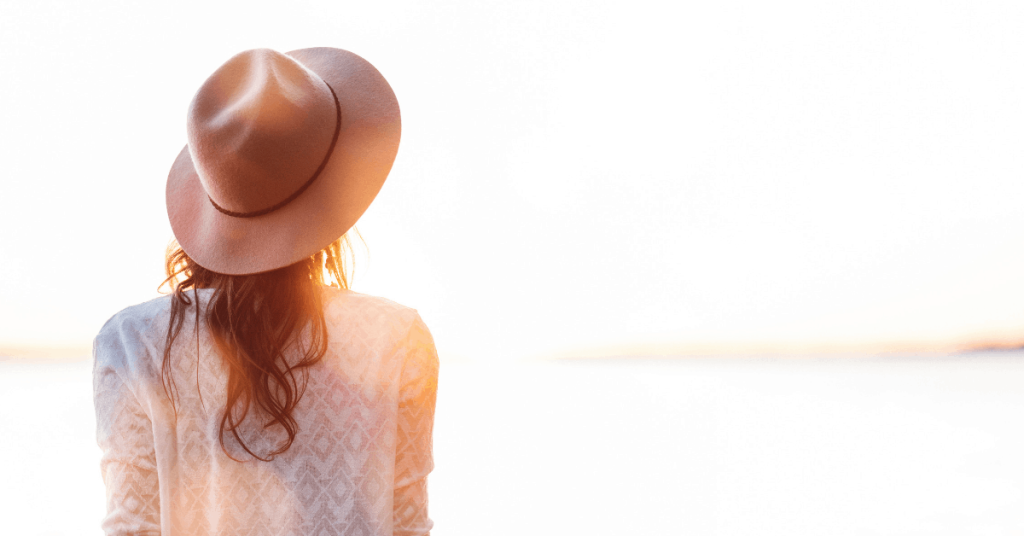 young woman in hat gazes out at water and bright sky
