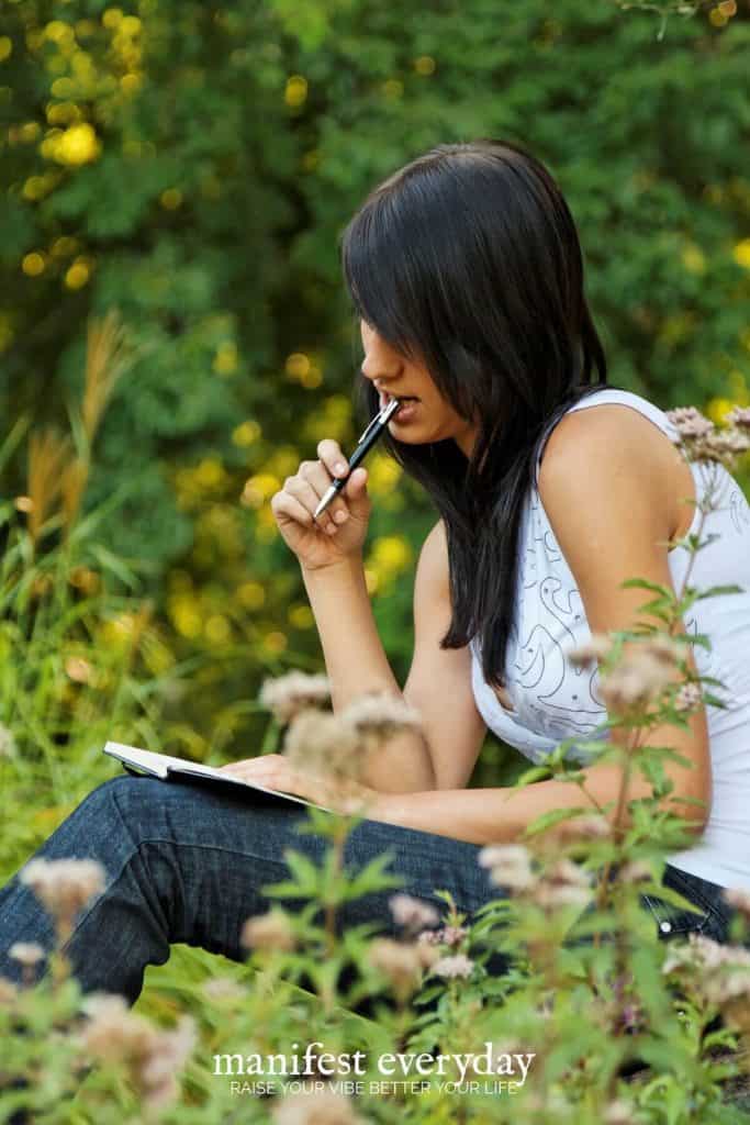woman sits in grass thinking and journaling her thoughts