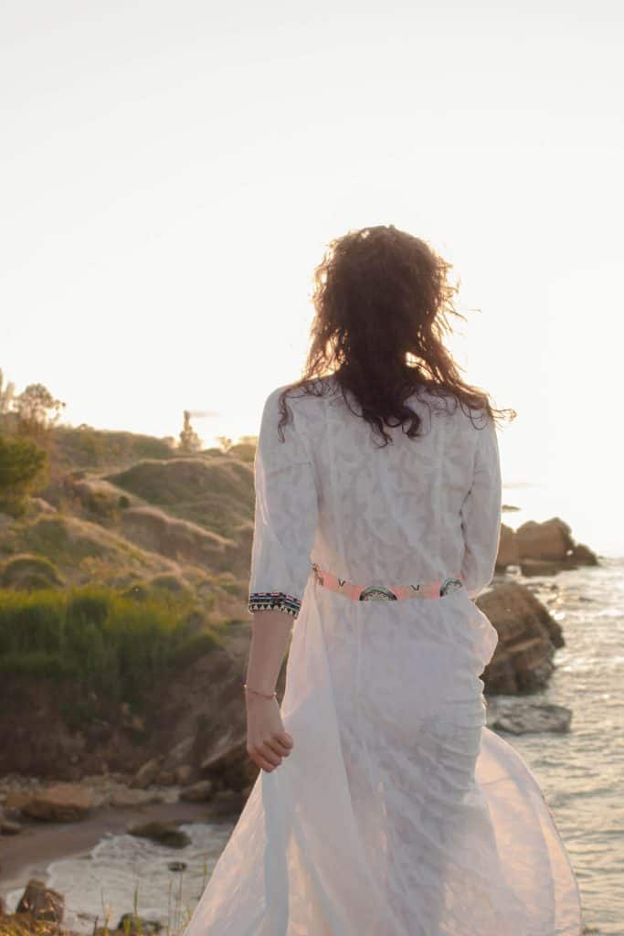 Young brunette woman in long white dress walking the beach early in the morning as the sun rises manifesteveryday.com
