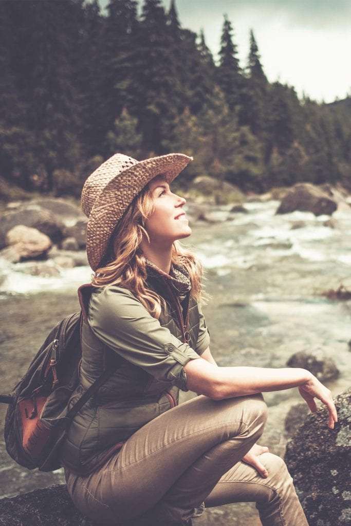 Young woman in straw cowboy hat sits on rocks and looks up at the sky