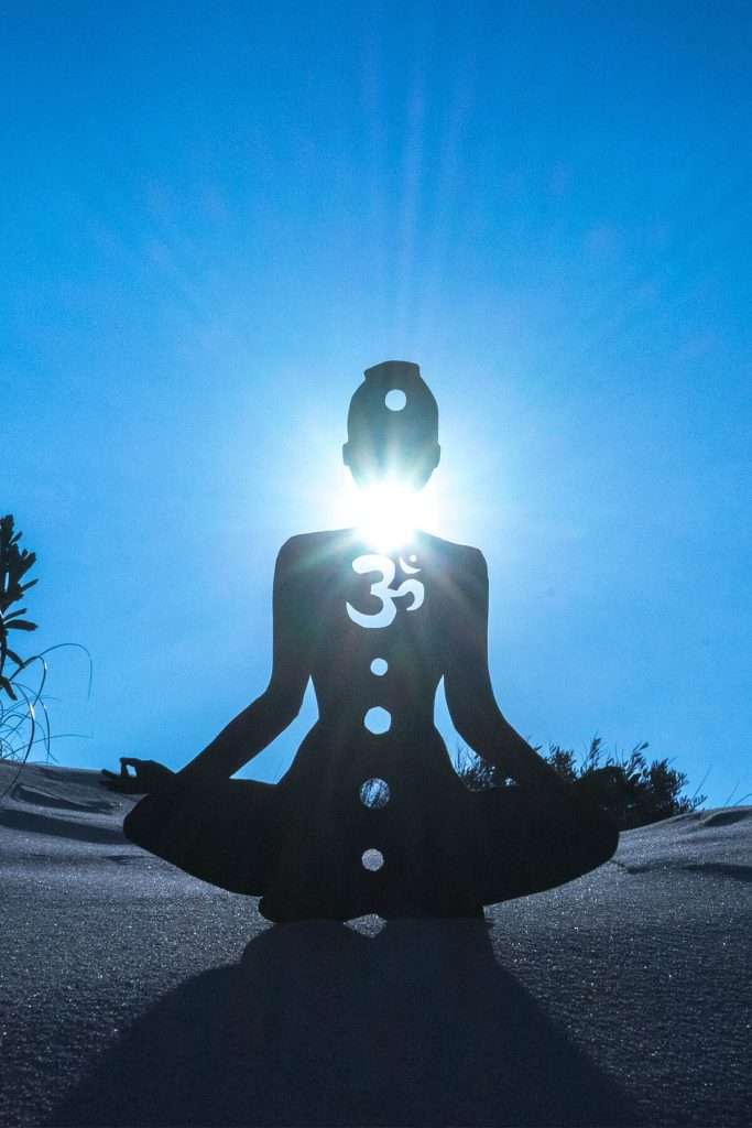 A silhouette of a person meditating with an open throat chakra under the sunlight manifesteveryday.com