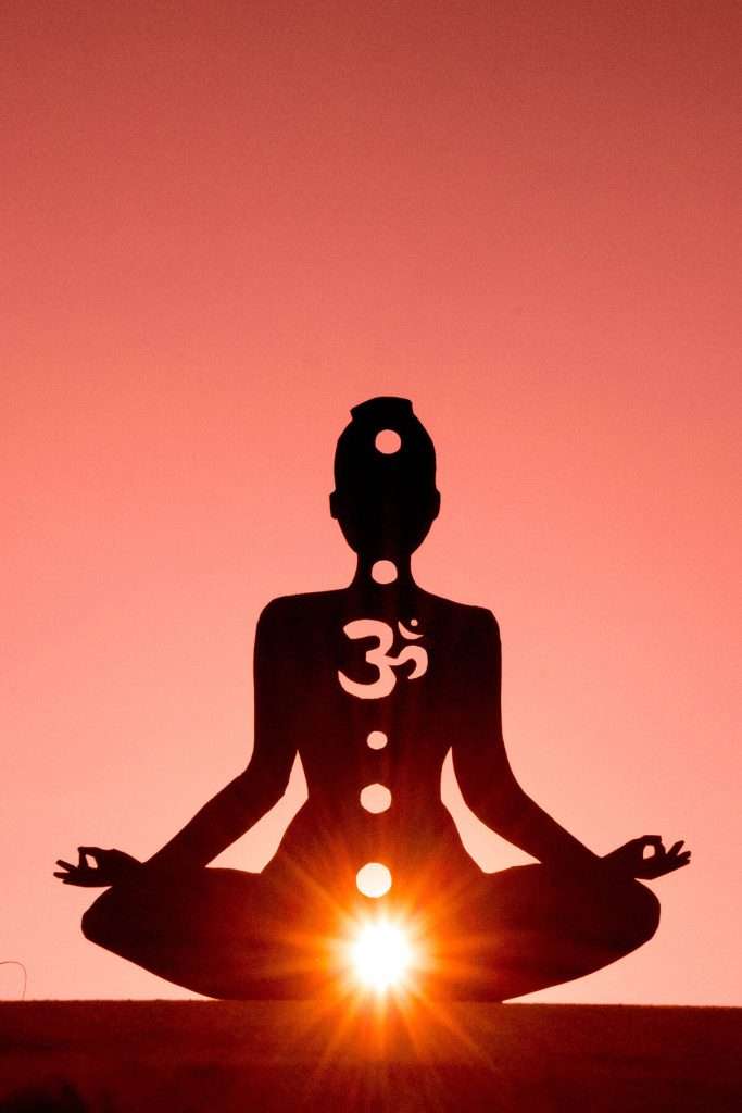 red background with silhouette of person meditating with mudras for the root chakra with the root chakra lit up
