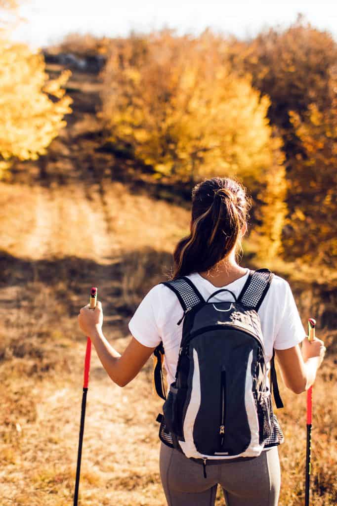 woman taking autumn hike with trekking poles on wooded trail
