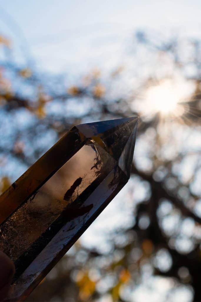smoky quartz crystal with trees and bright sun in the background
