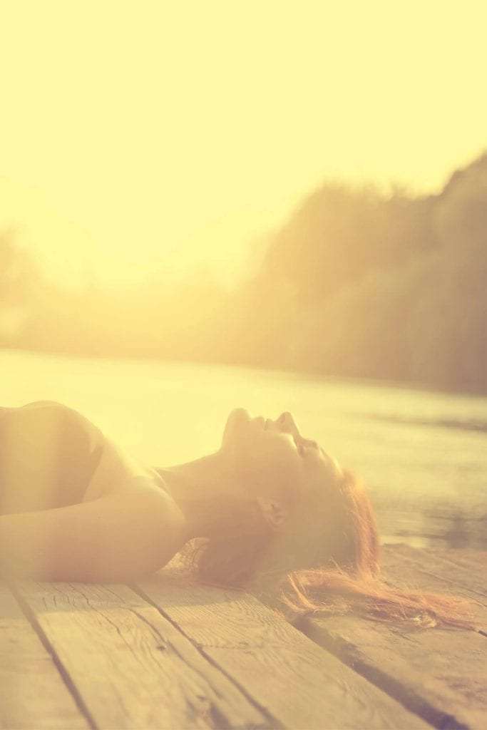 young woman lying on dock with eyes closed at sunset