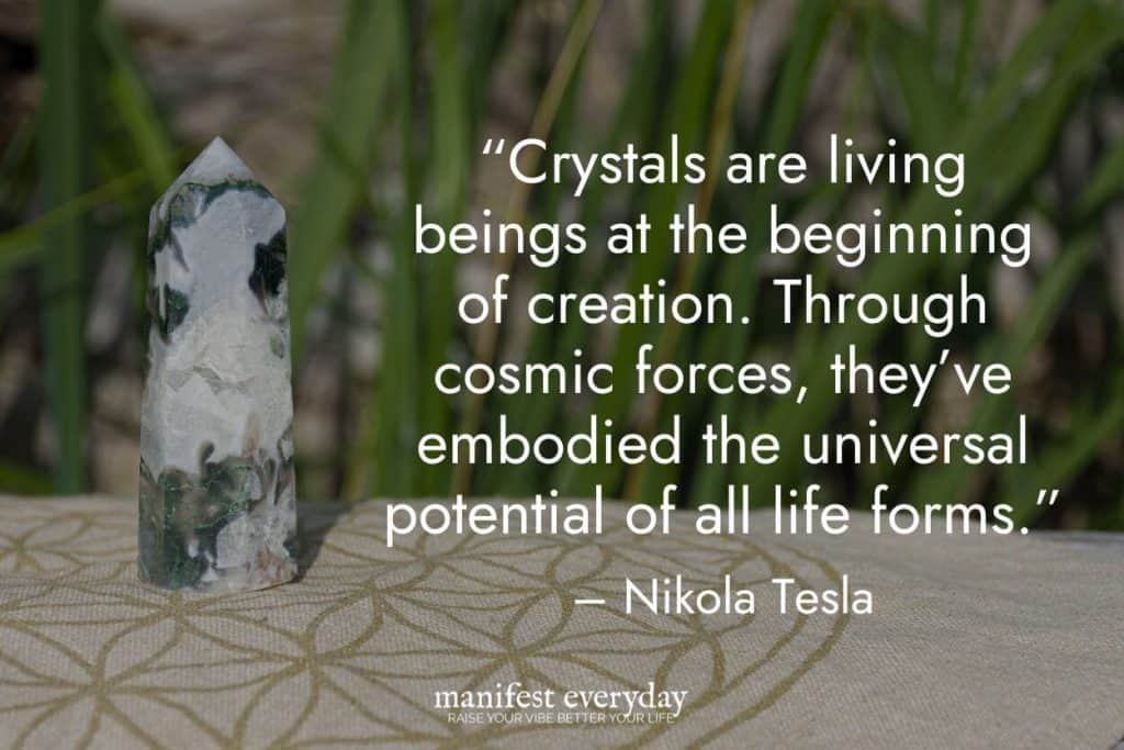 a crystal tower on a table with greenery in the background with quote text that reads “Crystals are living beings at the beginning of creation. Through cosmic forces, they’ve embodied the universal potential of all life forms.” - Nikola Tesla manifesteveryday.com