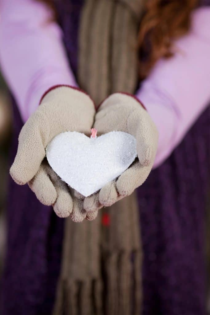 A child's gloved hands holding a heart-shaped piece of ice, symbolizing winter love and care.