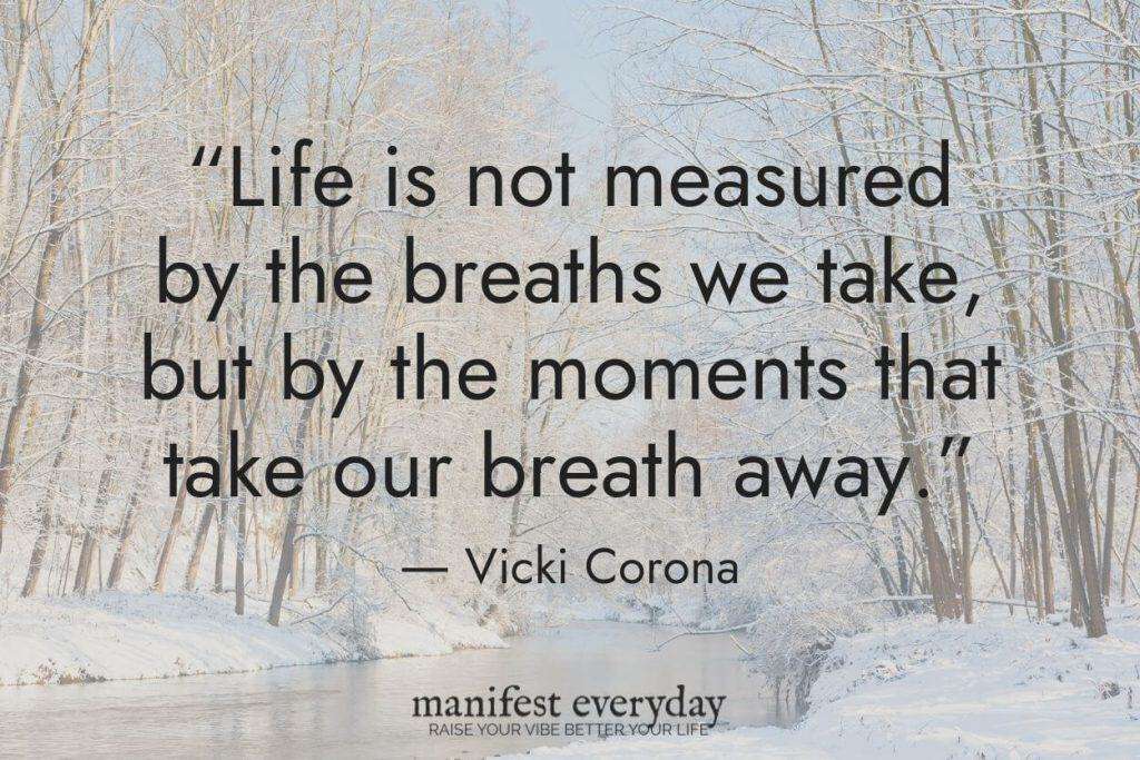 a bright winter scene of a river with snow covered backs and frosty trees with quote text that reads “Life is not measured by the breaths we take, but by the moments that take our breath away.” - Vicki Corona manifesteveryday.com