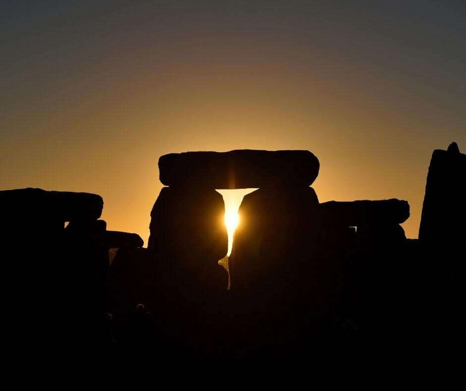 Dramatic spring equinox sunrise at Stonehenge with sun perfectly aligned between ancient stone trilithons, creating a powerful silhouette against golden dawn sky