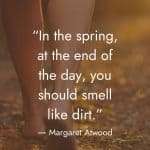 An inspirational quote by Margaret Atwood in white text overlaid on a close-up image of a woman's bare legs standing in leaves on the ground: "In the spring, at the end of the day, you should smell like dirt." manifesteveryday.com
