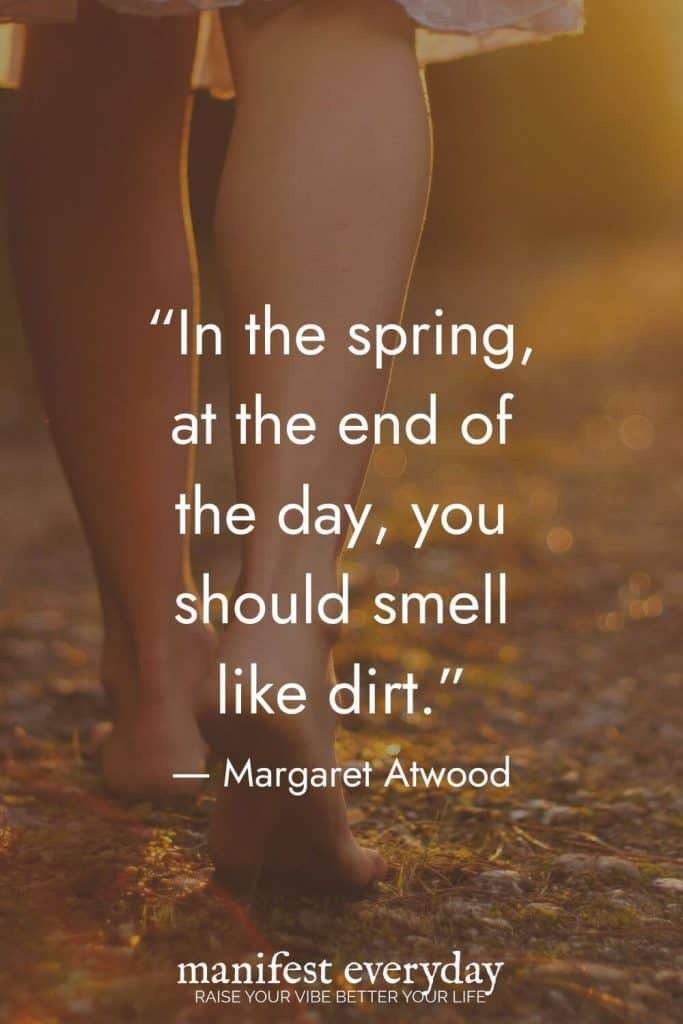 An inspirational quote by Margaret Atwood in white text overlaid on a close-up image of a woman's bare legs standing in leaves on the ground: "In the spring, at the end of the day, you should smell like dirt." manifesteveryday.com