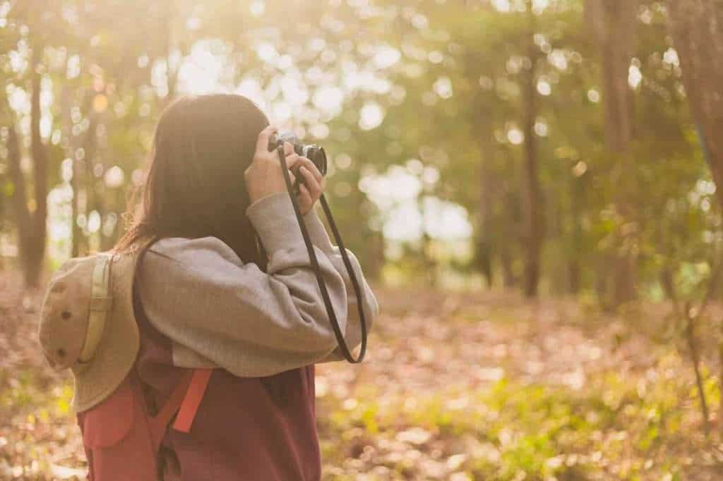 A woman with a backpack is taking a picture in the woods.
