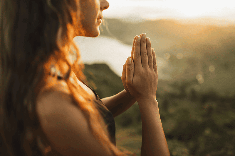 Close-up of hands in prayer position during golden hour for manifestation prayer and spiritual connection