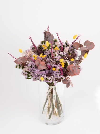 Flores frescas y elegantes en ramo con eucalipto y flores lilas en jarrón de cristal.