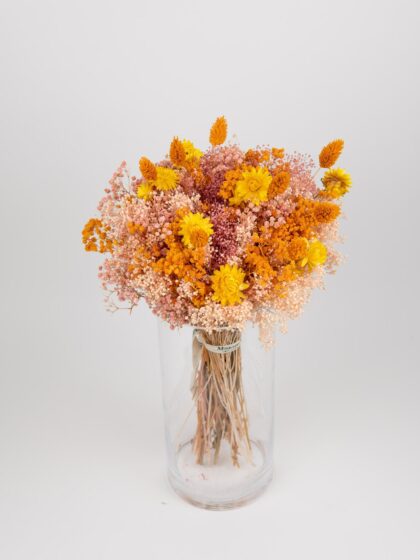 Ramo de flores secas en jarrón de cristal con tonos amarillos y naranjas vibrantes.