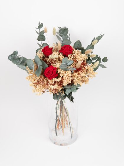 Ramo de flores con rosas rojas, eucalipto y flores secas en jarrón de cristal.
