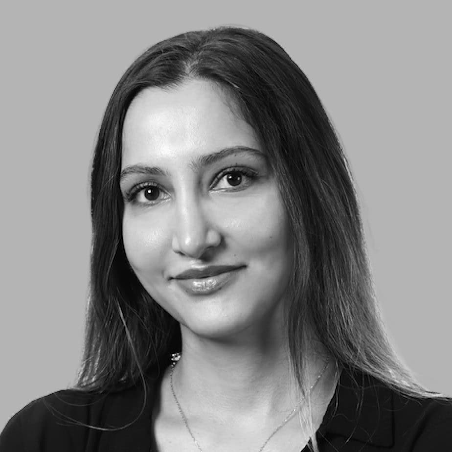 A woman with long hair smiles slightly at the camera against a gray background, exuding the calm confidence of a skilled marketing butler. She is wearing a dark top and a necklace.