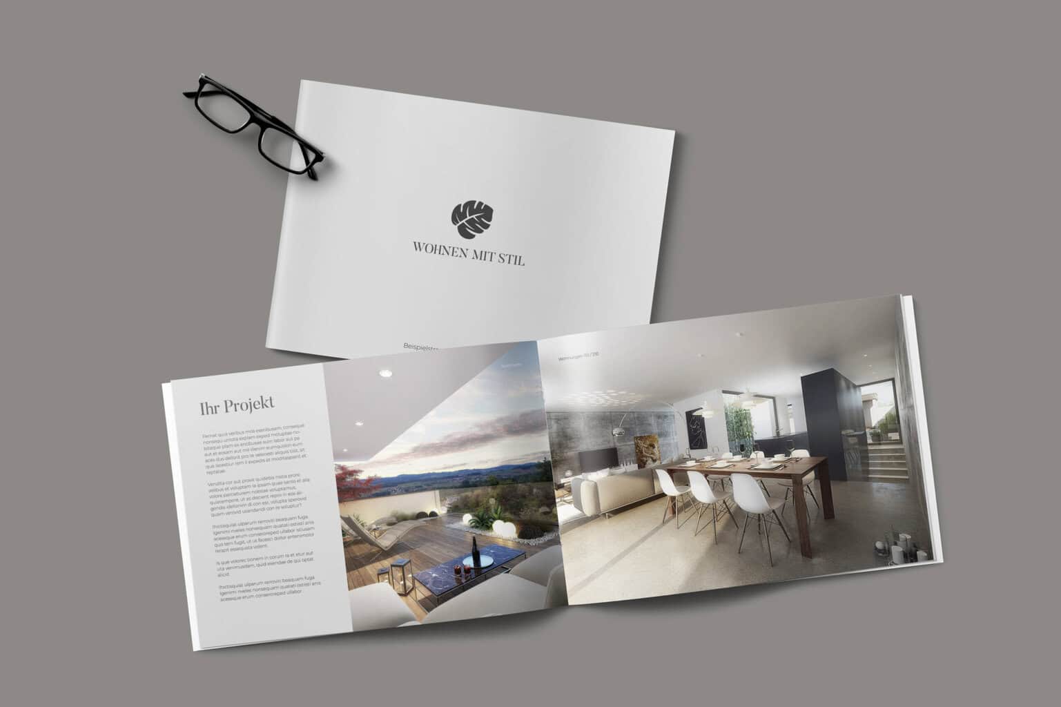 Auf dem Tisch liegt ein aufgeschlagenes Magazin mit Bildern und Texten zum Thema Innenarchitektur, daneben eine geschlossene Ausgabe mit dem Titel „Wohnen mit Stil“, daneben eine Brille. Es ist, als hätte eine elegante Broschürensammlung die Geheimnisse des stilvollen Wohnens dargelegt.