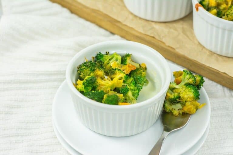 3 ingredient broccoli cheese casserole in a white ramekin on a plate with a fork piercing a portion of broccoli