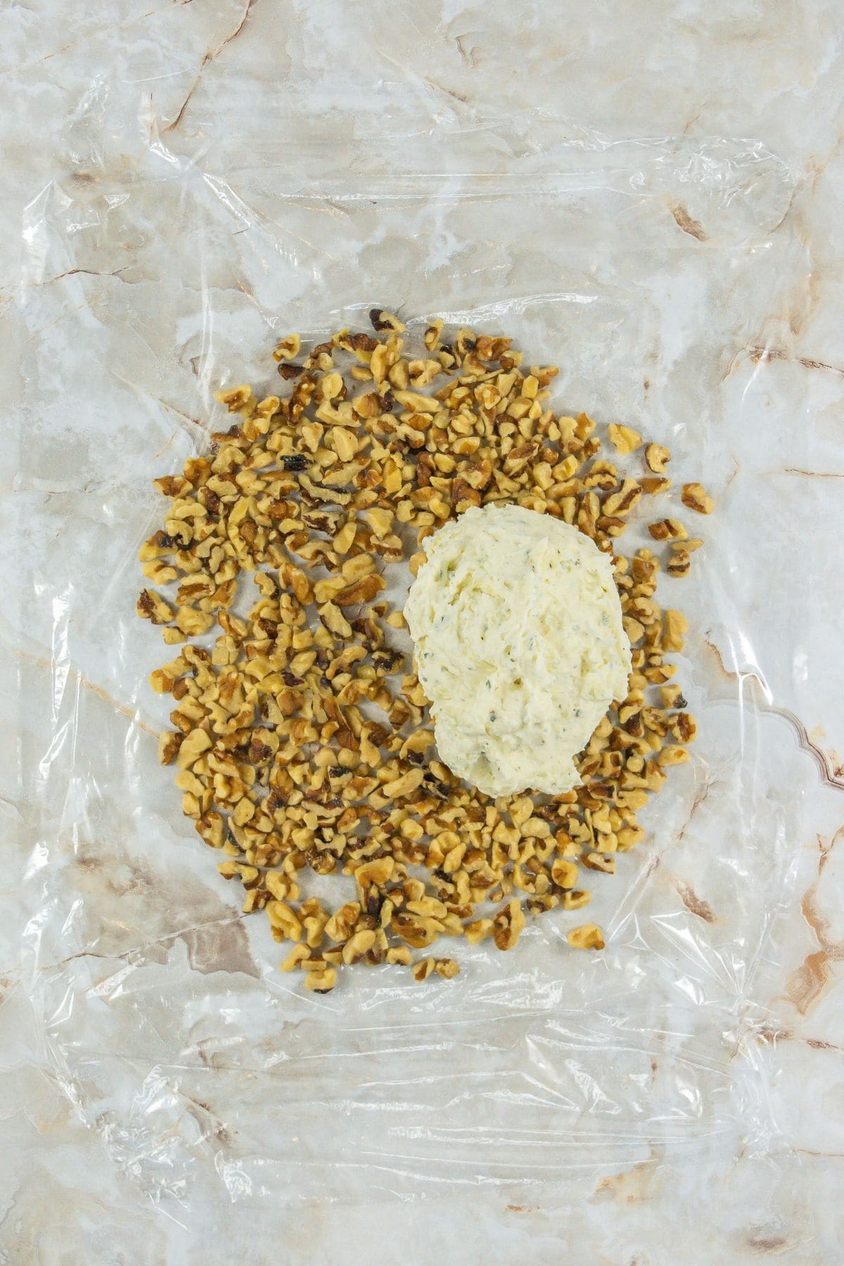 ball of cheese mixture placed on a layer of chopped walnuts in the middle of a plastic wrap