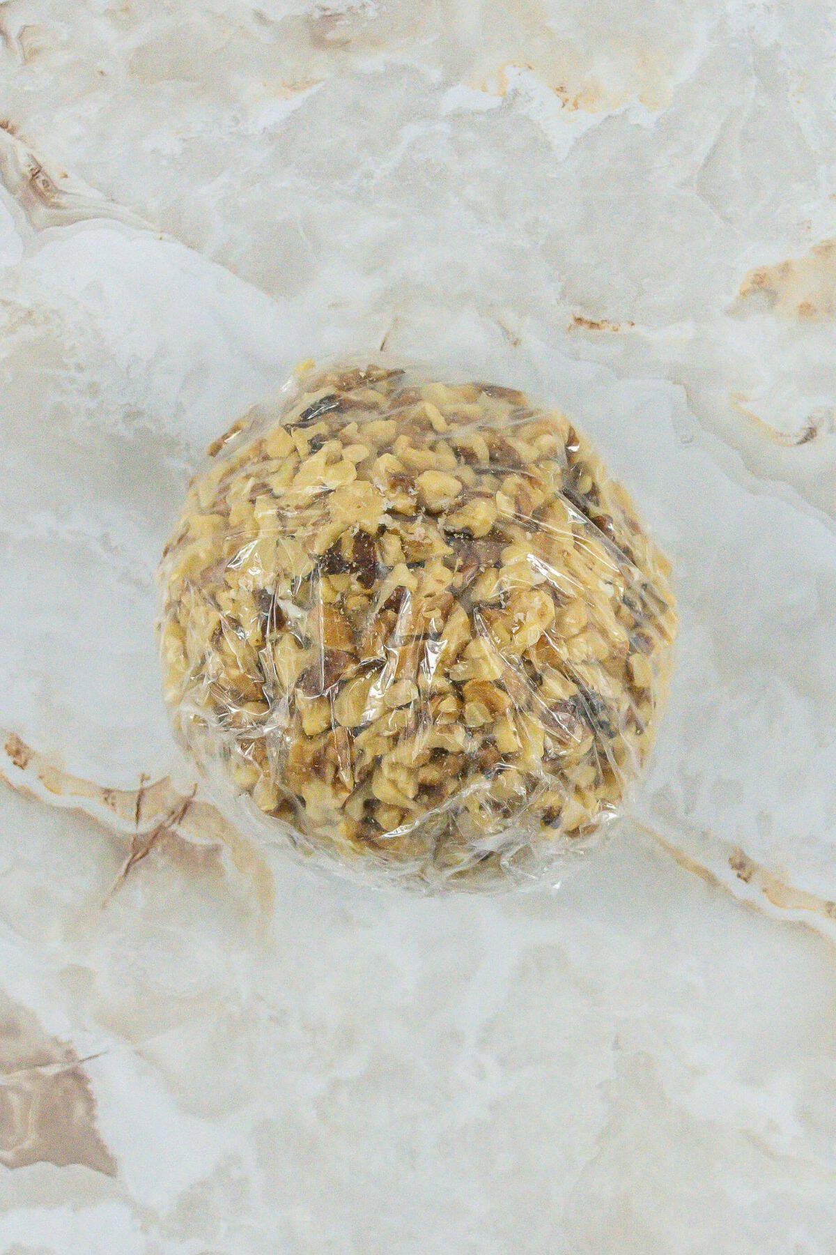 entire ball of cheese covered in walnuts wrapped in the plastic wrap