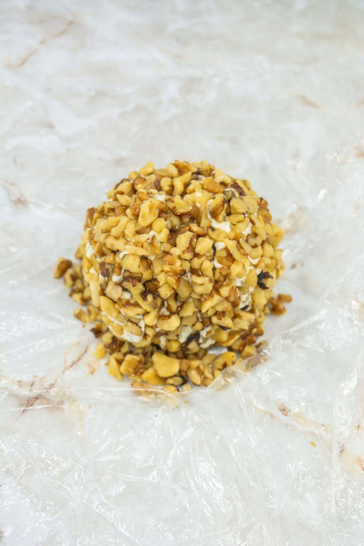 a cheese ball covered in walnuts on a plastic wrap