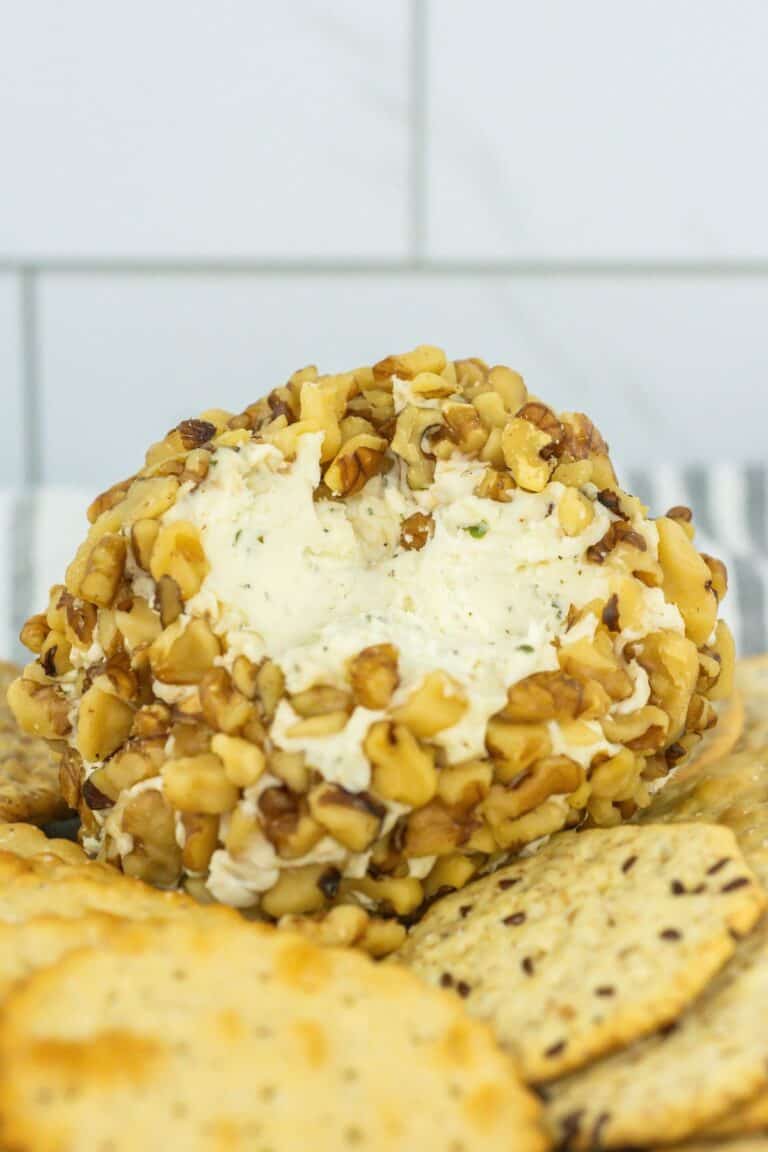 close-up of crackers and cheese ball covered in walnuts with a portion scooped out