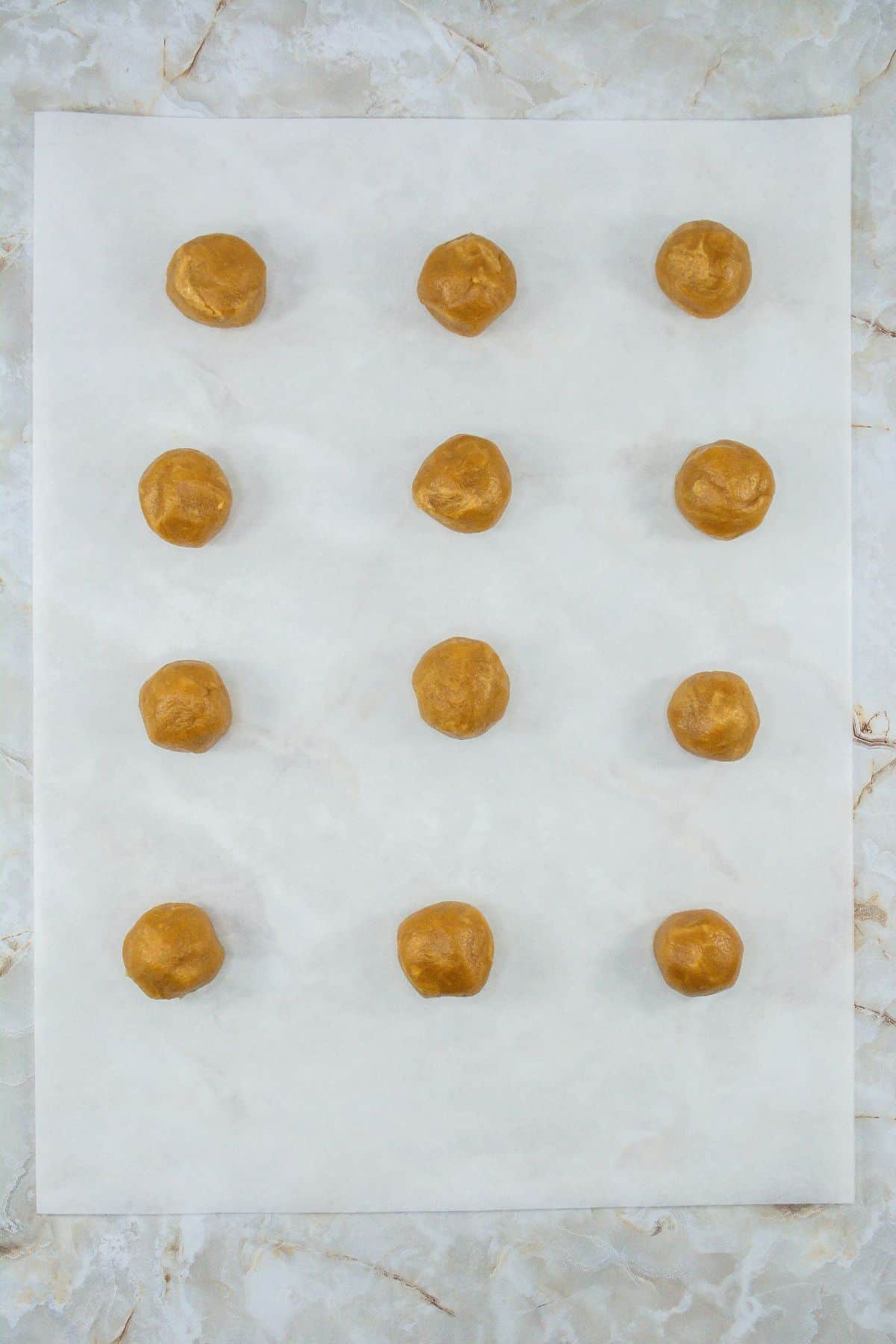 twelve peanut butter cookie doughs in about ping pong ball size arranged on a baking sheet
