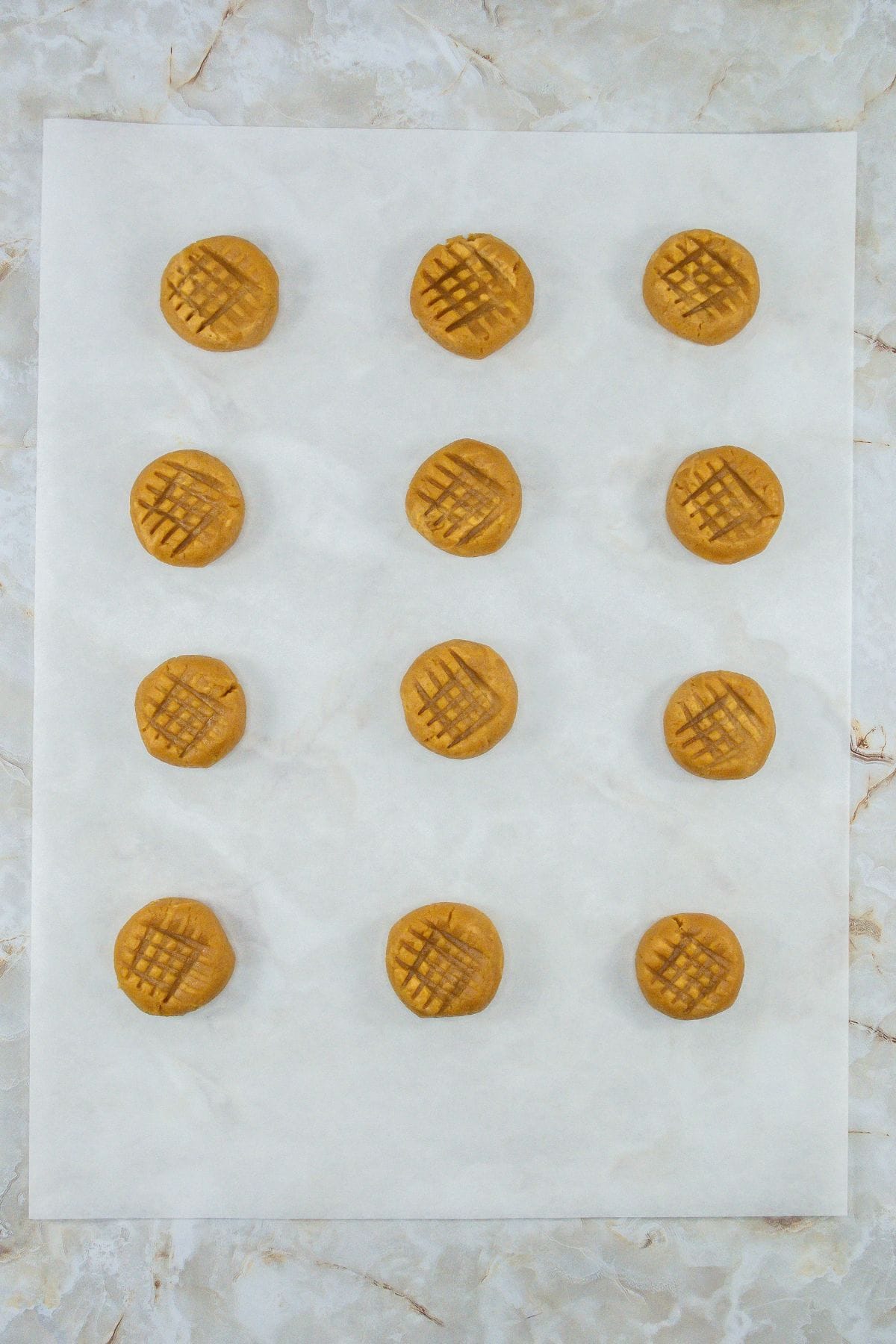 twelve pressed peanut butter cookie doughs arranged on a baking sheet